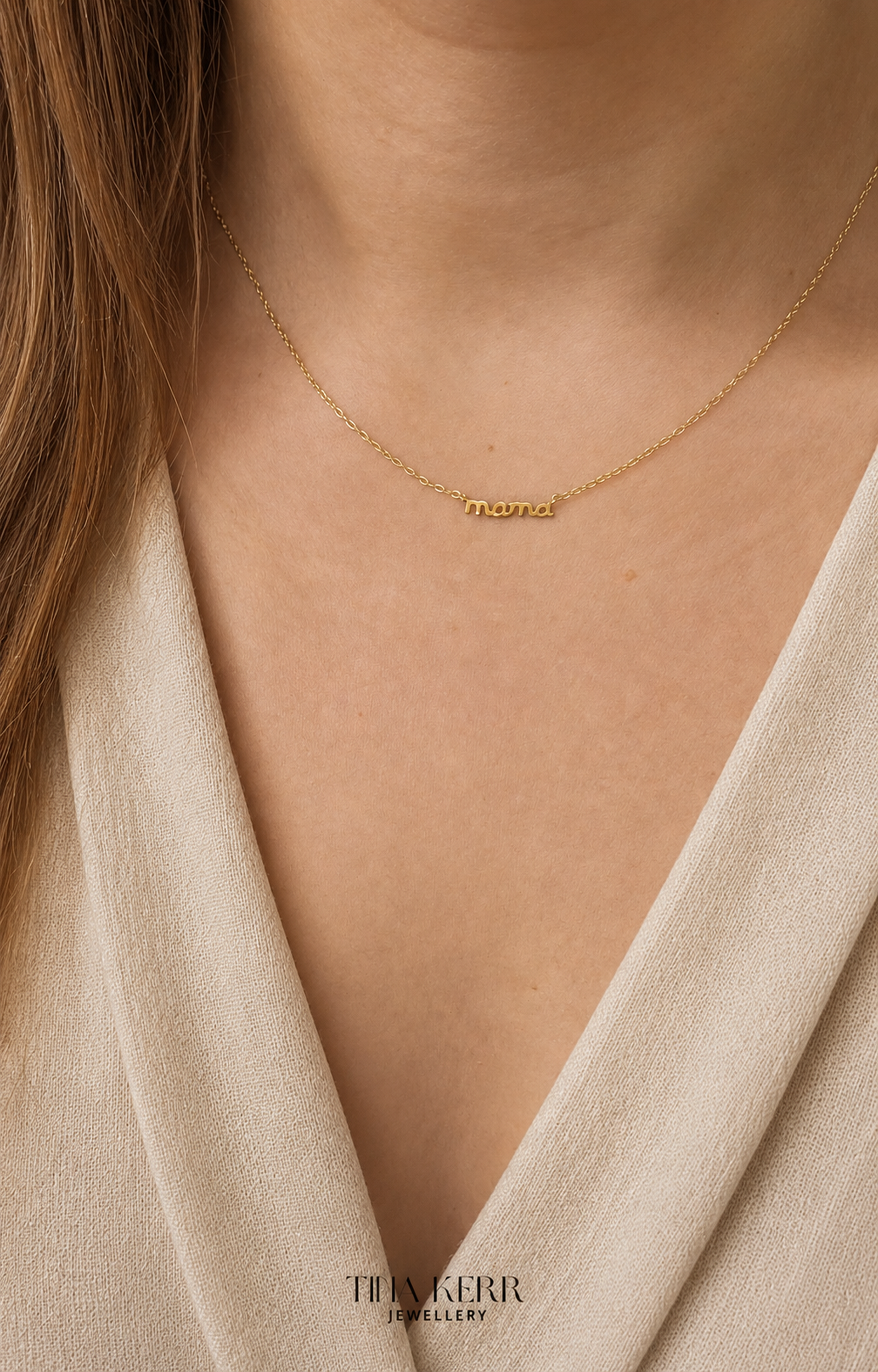 Gold necklace with a name pendant on a person wearing a beige top, branded 'Tilly Kerr Jewellery'.