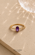 Gold ring with an amethyst stone on a beige surface, branded 'Tina Kerr Jewellery'.