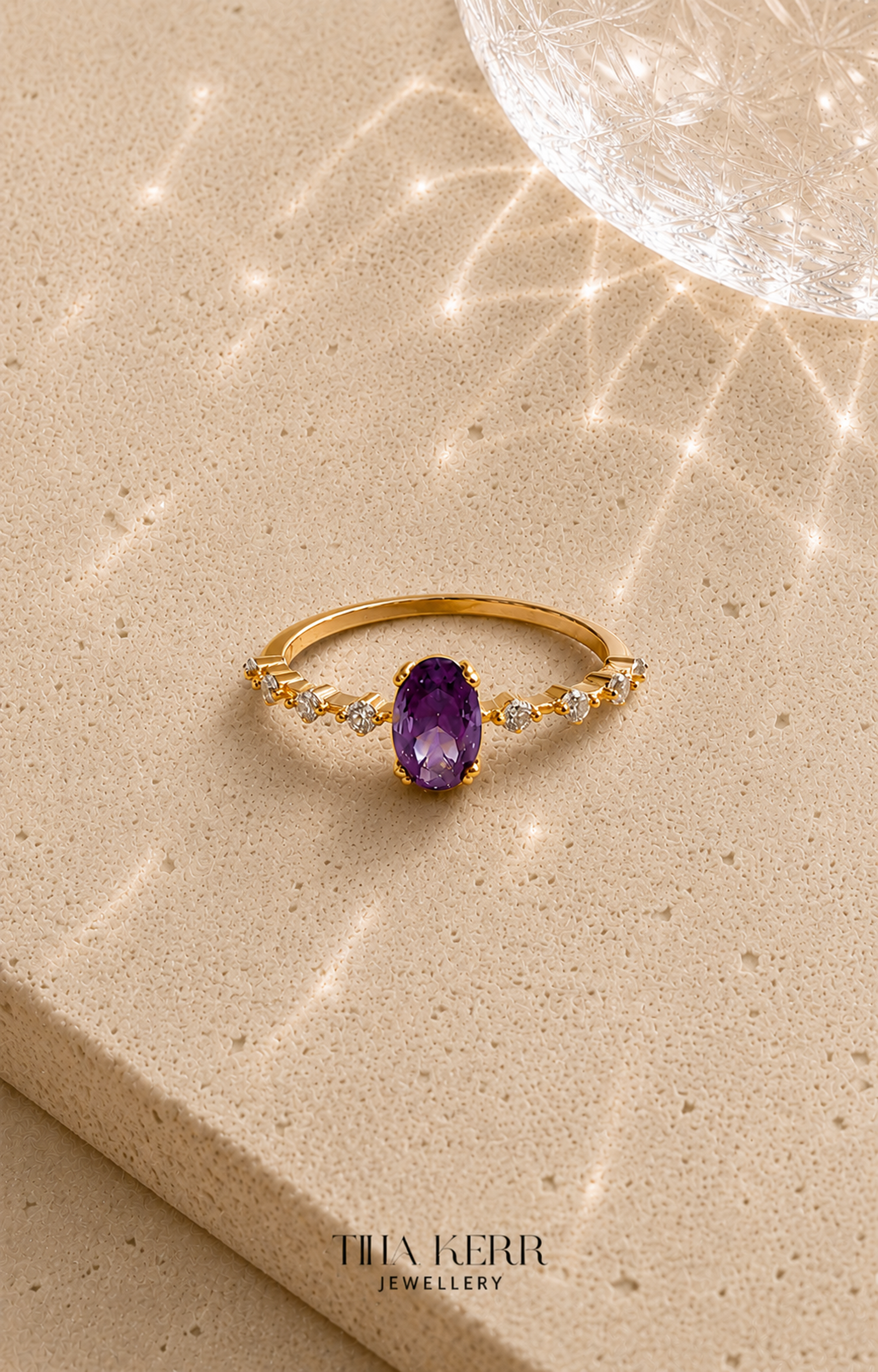 Gold ring with an amethyst stone on a beige surface, branded 'Tina Kerr Jewellery'.